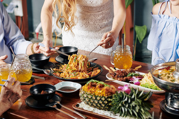 Obraz na płótnie Canvas Cropped image of housewife serving food at dinner table with various delicious dishes of Asian cuisine
