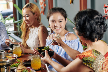 Smiling pretty preteen girl enjoying tasty dinner with her family in restaurant