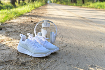 White sneakers, a bottle of water and headphones, a set for running in the woods on a forest road.