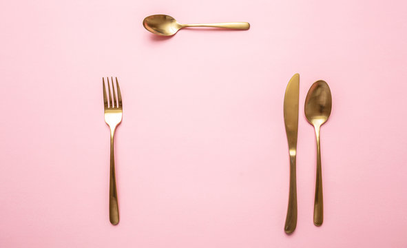 Gold cutlery set against pink background, formal place setting