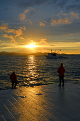 Incredible sunset (sunrise, dawn) at sea with silhouettes of people (couple) and a boat in Zadar (Croatia)