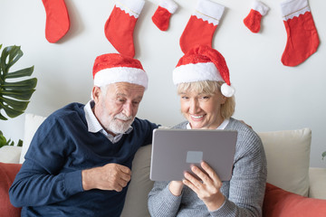 senior elderly caucasian old man and woman, using conference on tablet with family together in living room that decorated for christmas festival day in the morning, retirement concept