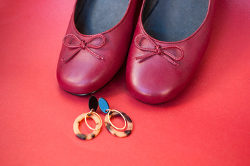 Stylish female flat shoes in dark red color and earrings with leopard print on dark red background. Beauty and fashion concept.