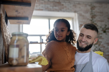Bearded father smiling while daughter dusting shelves