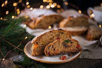 A traditional German Christmas Stollen lies on a wooden table. A celebratory cake is cut into slices with candied fruits, nuts and raisins. Selective focus.