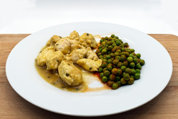  Chicken curry served with green peas served in a white dish, wooden table, white background.