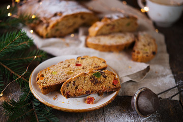A traditional German Christmas Stollen lies on a wooden table. A celebratory cake is cut into slices with candied fruits, nuts and raisins. Selective focus.