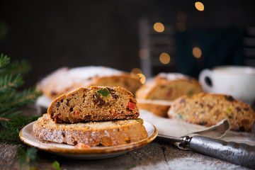 A traditional German Christmas Stollen lies on a wooden table. A celebratory cake is cut into slices with candied fruits, nuts and raisins. Selective focus.