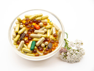 A transparent bowl full of pills and pills, a sprig of yarrow beside it.