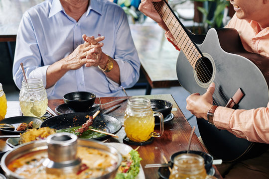 Cropped image of smiling Asian man playing guitar at dinner with his senior father