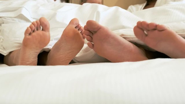 Family resting in a hotel. The bare feet of the couple lies on the bed.