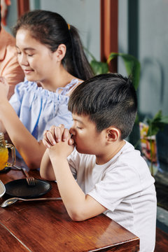 Adorable little Asian boy and his preteen sister praying before having meal at home