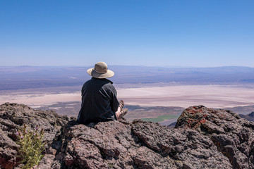 Young woman in a stray hat sitting on a cliff overlooking Alvord Desert. Steens Mountains, south Oregon