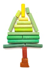Christmas tree from pastel chalk, vivid vibrant green, yellow, brown crayon sticks aligned on white background, creativity colorful kid's art supplies in classroom, children's activity in holiday.