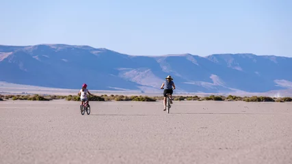 Fotobehang A woman on a bike and a little boy on a balance bike ride o a playa of Alvord lake against Steens mountains in the background © Dmitry