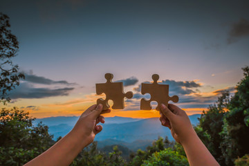 A businessman connects a jigsaw puzzle on a sunrise in the background as a business collaboration,...