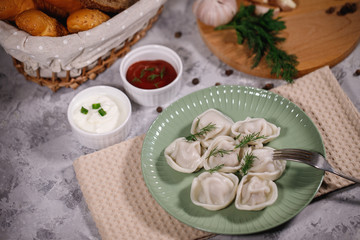 Ravioli on a plate with dill, served with sauce and ketchup. Boiled dumplings on a dish. Tasty dinner. Food. Close-up.
