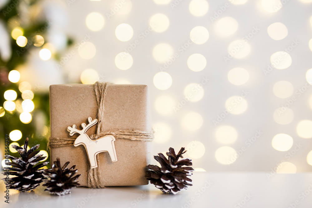 Wall mural close up of gift box and fir cones near decorated christmas tree over white wall background with lig