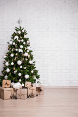 christmas and new year background - christmas tree and gift boxes over white brick wall with copy...