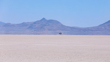 Car speeding on a playa of Alvord Lake, South Oregon. A trace of dust rises behind a car driving fast on hot day. Warm air creates a mirage of a water on a surface of a dried lake