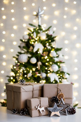 christmas and new year concept - beige gift boxes near decorated christmas tree over white wall with lights