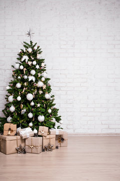 christmas and new year background - christmas tree and gift boxes over white brick wall with copy space