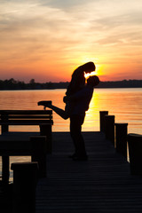 Vertical portrait of a loving romantic couple making their engagement announcement at the end of a pier at sunset