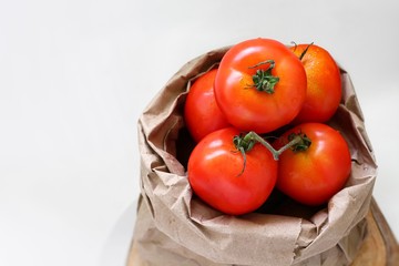Tomato in brown paper bag isolated on white background, copy space, natural light, group of red tomatoes vegetable fruits in eco package