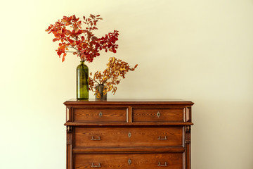Wooden chest of drawers with floral branches in vase