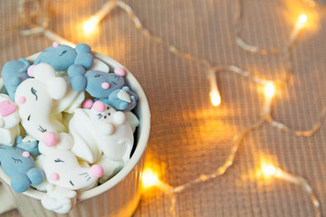Cup of chocolate, marshmallow in gray and white mouse or rat shape, warm knitted sweater. Warm lights. Cozy winter morning. Lifestyle concept. Selective focus.
