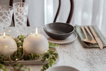 Fototapeta na wymiar Scandinavian style minimalist Christmas table setting , grey white plate, linen napkin, gold cutlery and eucalyptus centrepiece with candle.