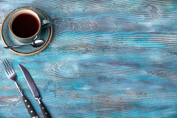 Hot coffee laid on a blue wooden background with knife and fork. Copy space