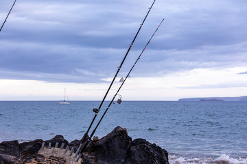 Fototapeta premium Fishing rods in a white stands on a side of a black rock against an ocean, Maui, Hawaii
