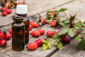Glass bottle of rosehip seed essential oil with fresh fruits on a wooden table. Tincture or essential oil with rose hips.