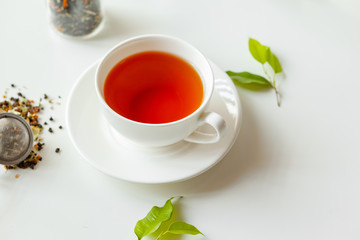 Cup of hot black tea on white table with dry tea jar