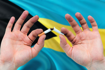 Bahamas quit smoking cigarettes concept. Adult man hands breaking cigarette. National health theme and country flag background.
