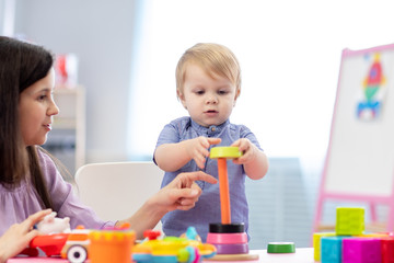Cute woman and kid toddler playing educational toys at kindergarten or nursery room