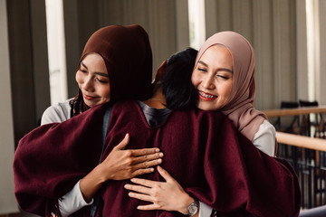 Cheerful Asian female in traditional Islamic hijabs smiling and embracing friend of different...