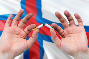 Faroe Islands quit smoking cigarettes concept. Adult man hands breaking cigarette. National health theme and country flag background.