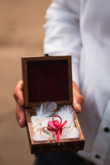 Man holding wedding rings in beautiful box tied with red ribbon.