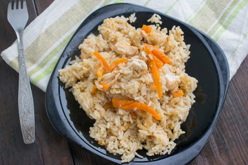 rice with meat and vegetables, top view, on a black plate, rustic style, wooden table and cotton towel