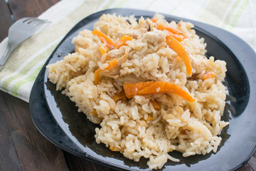 rice with meat and vegetables in a black plate on a wooden background