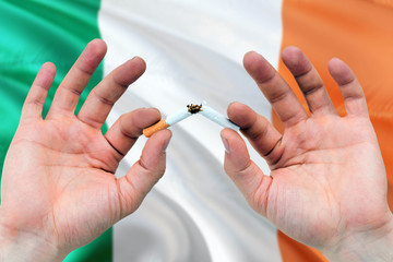 Ireland quit smoking cigarettes concept. Adult man hands breaking cigarette. National health theme and country flag background.
