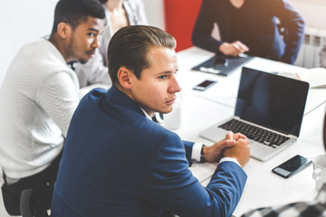 A team of young office workers, businessmen with laptop working at the table, communicating together in an office. Corporate businessteam and manager in a meeting. coworking.