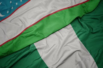 Obraz premium waving colorful flag of nigeria and national flag of uzbekistan.