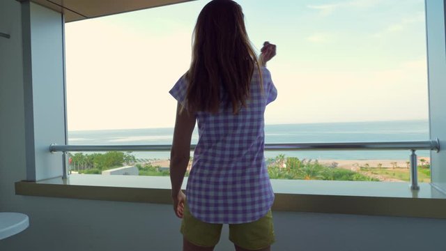 Girl dancing lambada and enjoying life on the balcony of the hotel overlooking the sea or ocean. View of the sandy beach. Travel and tourism concept.