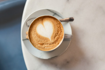 One cup of cappuccino with latte art on white table, white ceramic cup, top view. Cafe culture.