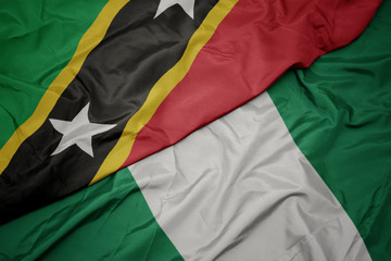 waving colorful flag of nigeria and national flag of saint kitts and nevis.