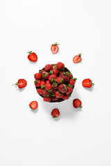 Slices of ripe strawberries around a bowl with ripe strawberries on a white surface. Top view.