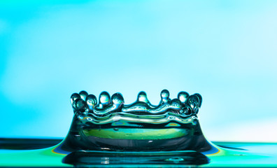 close up of a falling water drop impacting on a body of water on a colorful background.